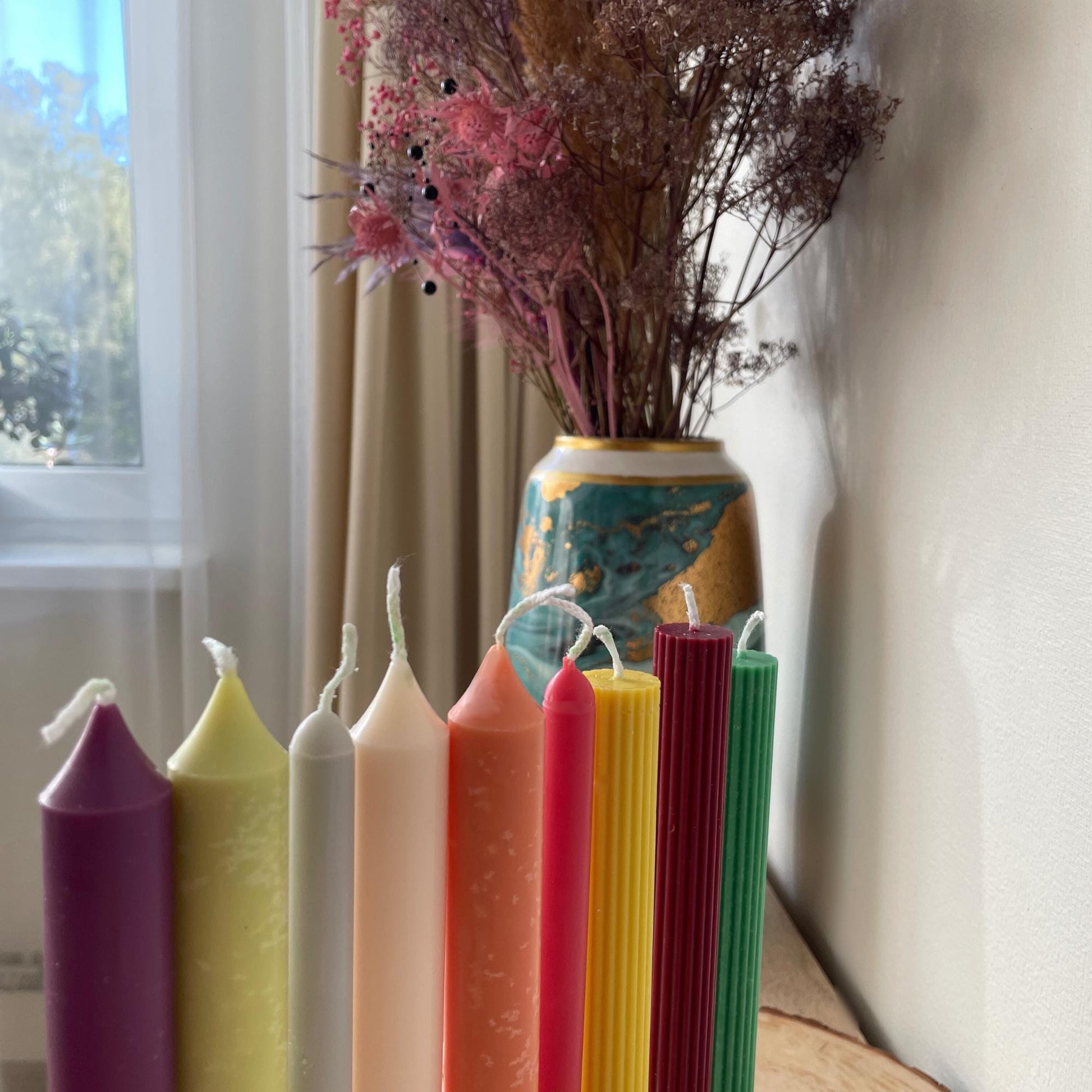 Colorful taper candles for dinner table in various colors standing next to a decorative vase with dried flowers