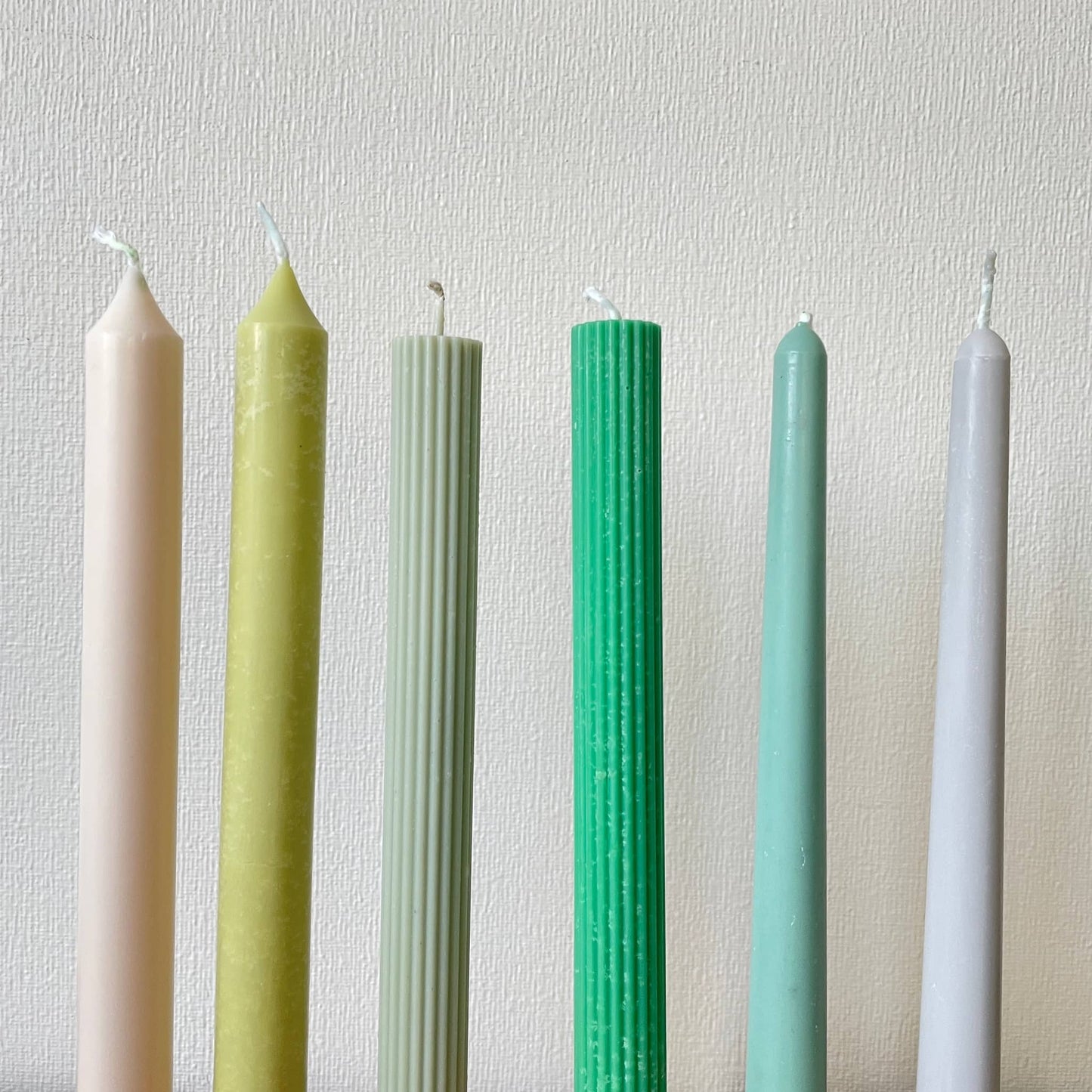 Colorful taper candles for dinner table by La Bouqe in pastel and muted green shades set against a white textured background
