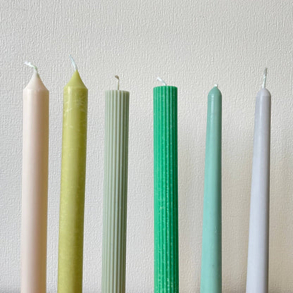 Colorful taper candles for dinner table by La Bouqe in pastel and muted green shades set against a white textured background