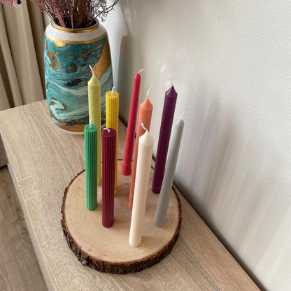 Colorful taper candles for dinner table displayed on wooden slice with decorative vase background