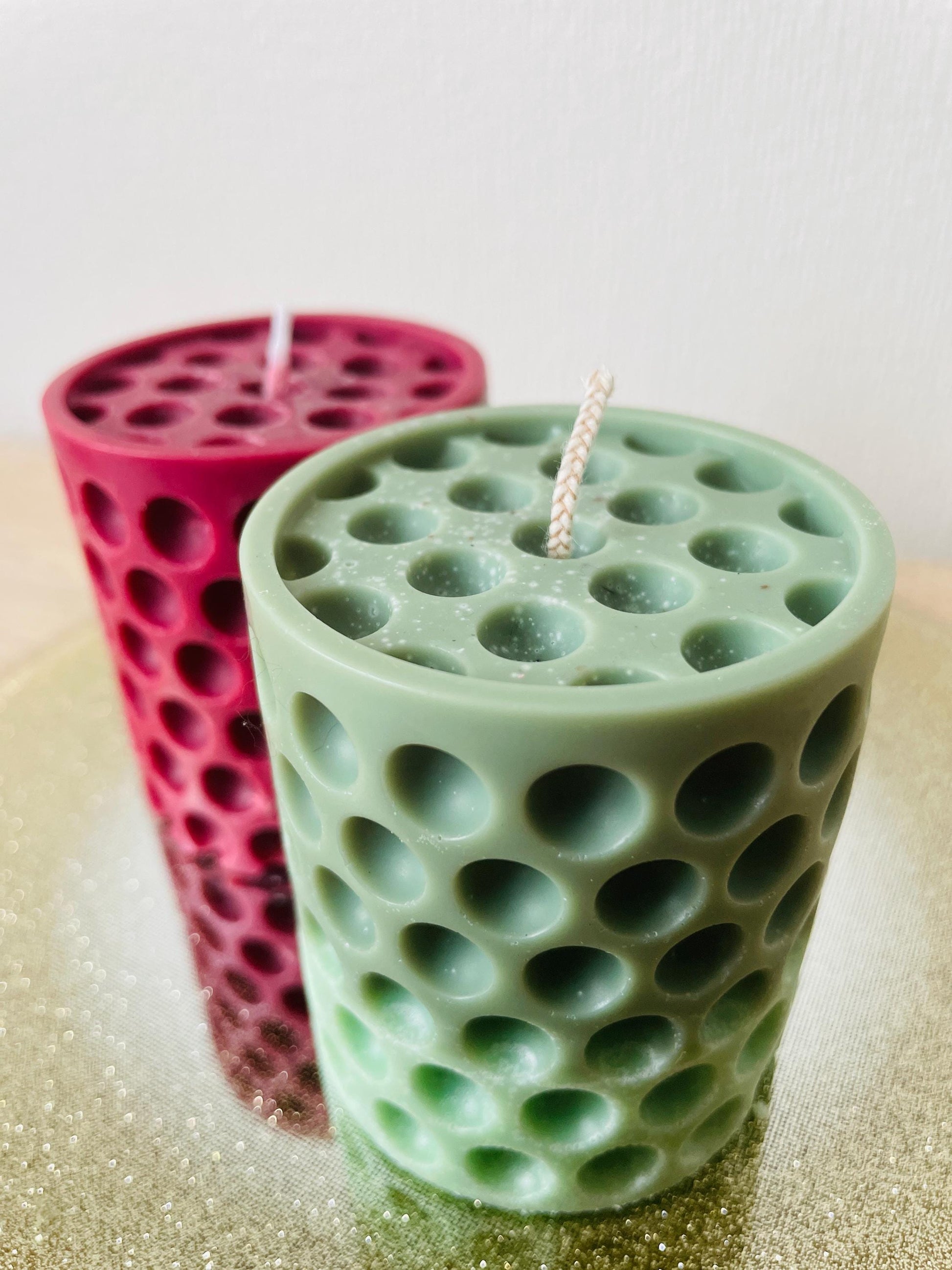Green and red La Bouqe dotted cylindrical handmade candle with multiple round indentations on a reflective surface