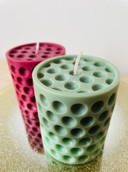 Green and red La Bouqe dotted cylindrical handmade candle with multiple round indentations on a reflective surface
