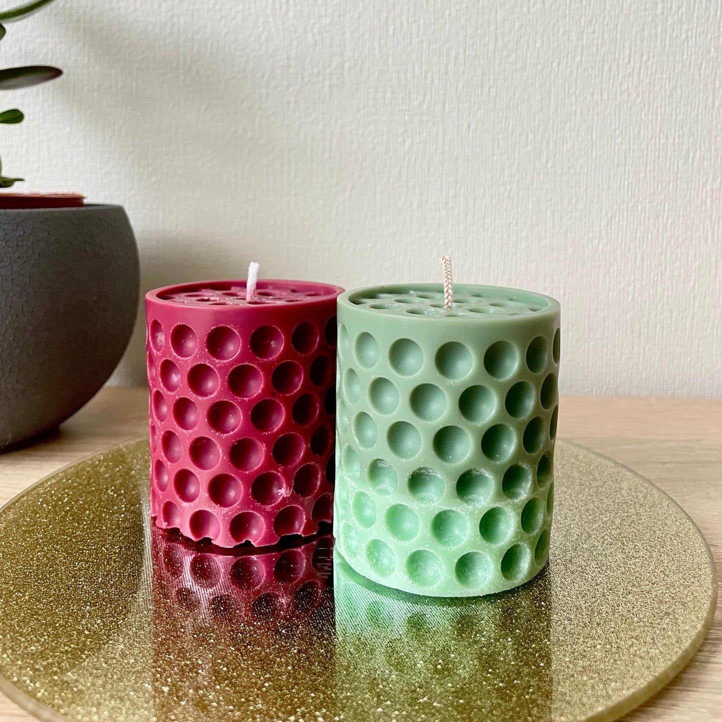 Red and green dotted cylindrical handmade candle set displayed on a gold glitter tray