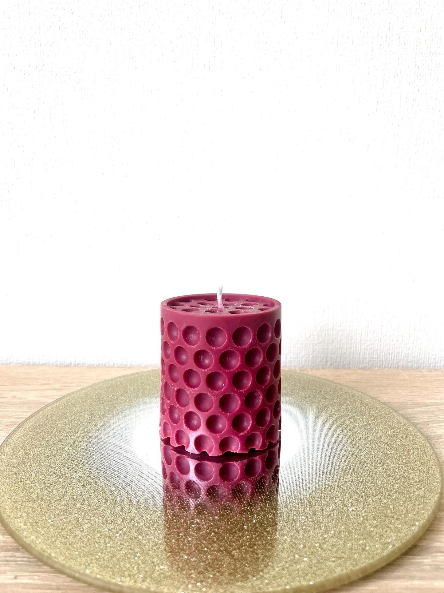 La Bouqe dotted cylindrical handmade candle in deep red placed on a reflective golden surface
