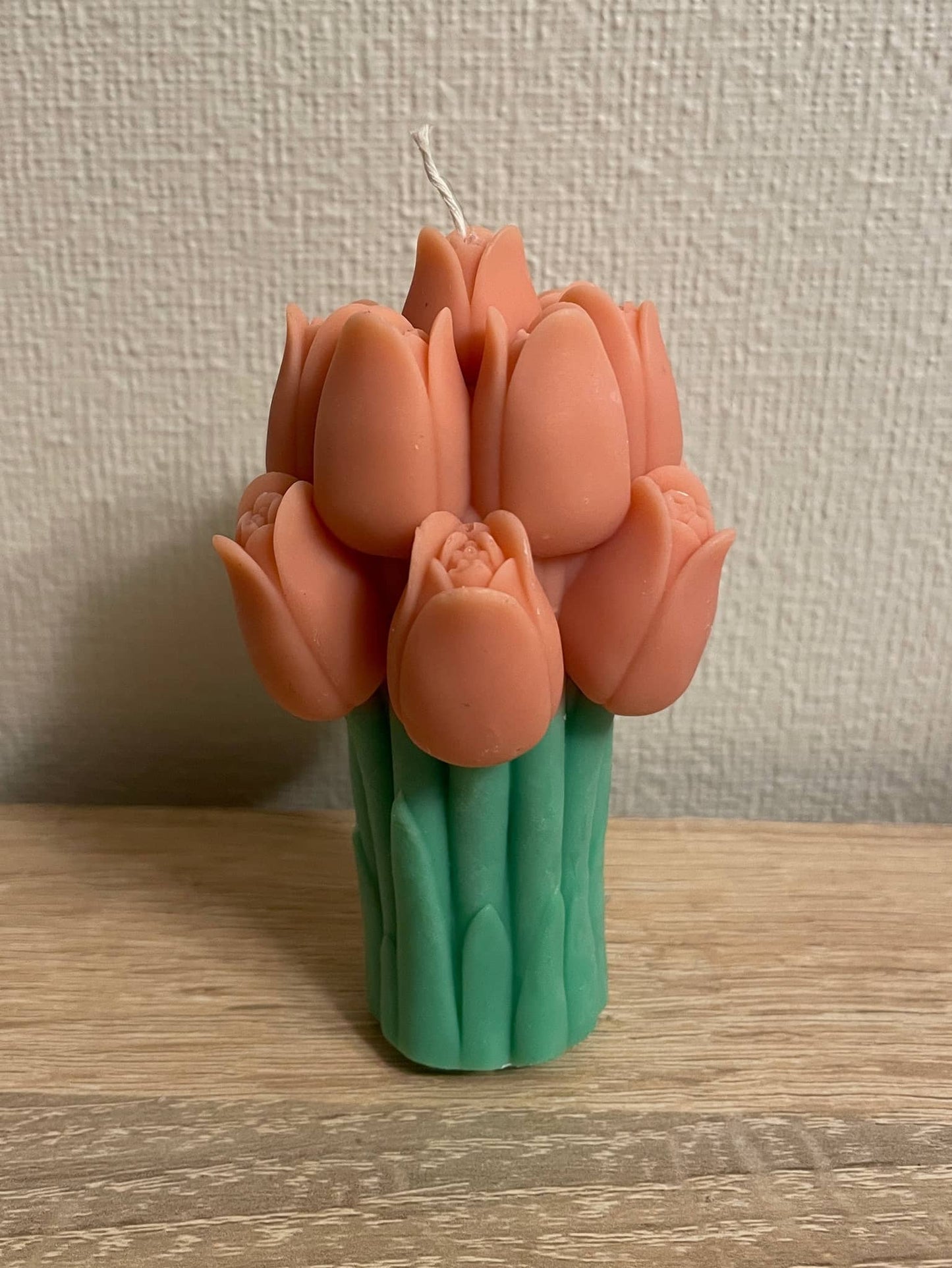 La Bouqe tulip bouquet candle with orange tulip-shaped wax flowers and green stems on wooden table
