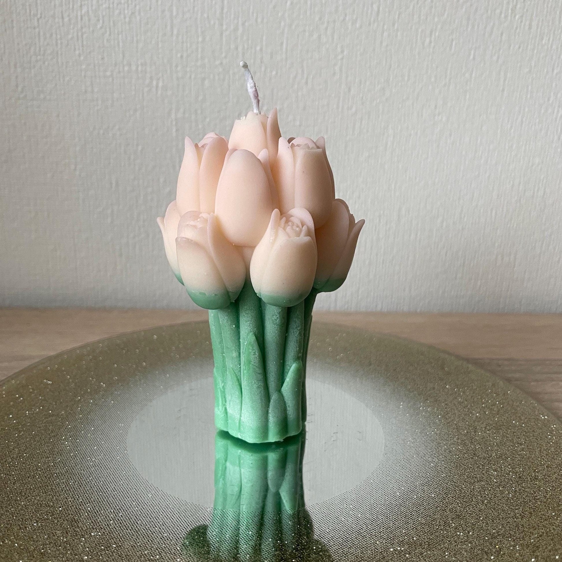 La Bouqe tulip bouquet candle with pale pink petals and green stems on a reflective surface